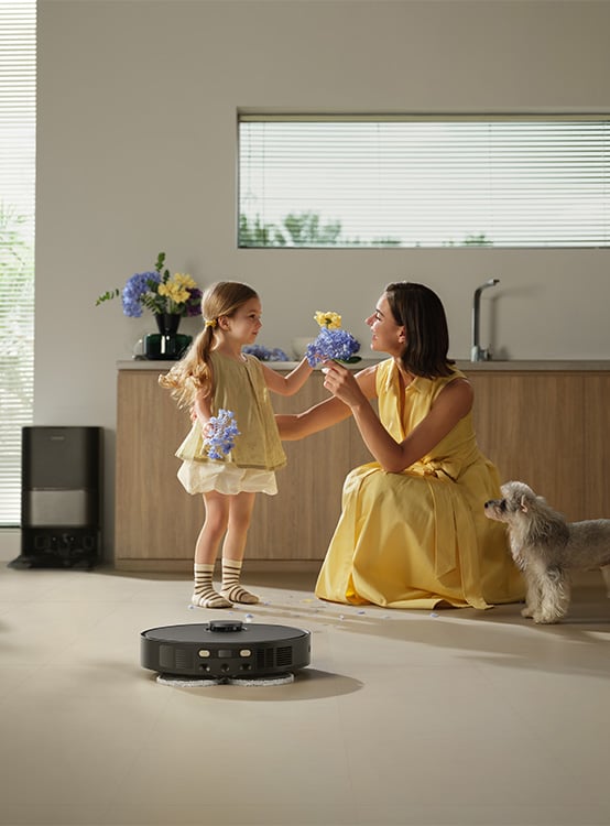 Mama, córka i mały pies, obok których sprząta czarny robot sprzątający